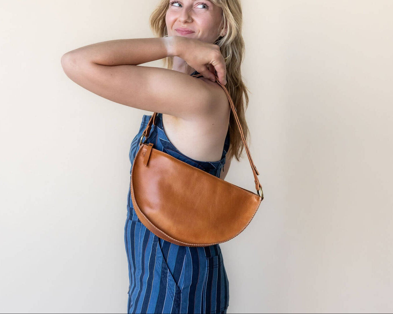 Woman holding a brown leather bag against a plain background