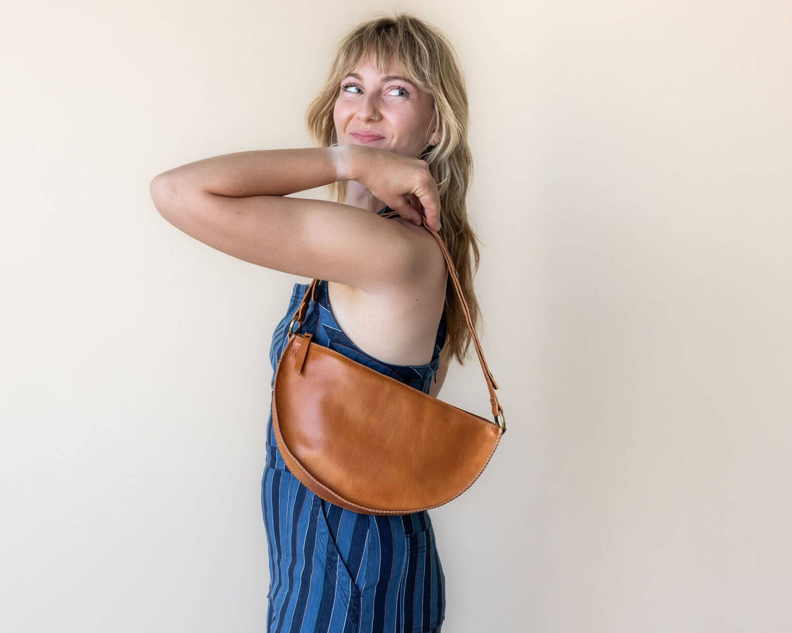 Woman holding a brown leather bag against a plain background