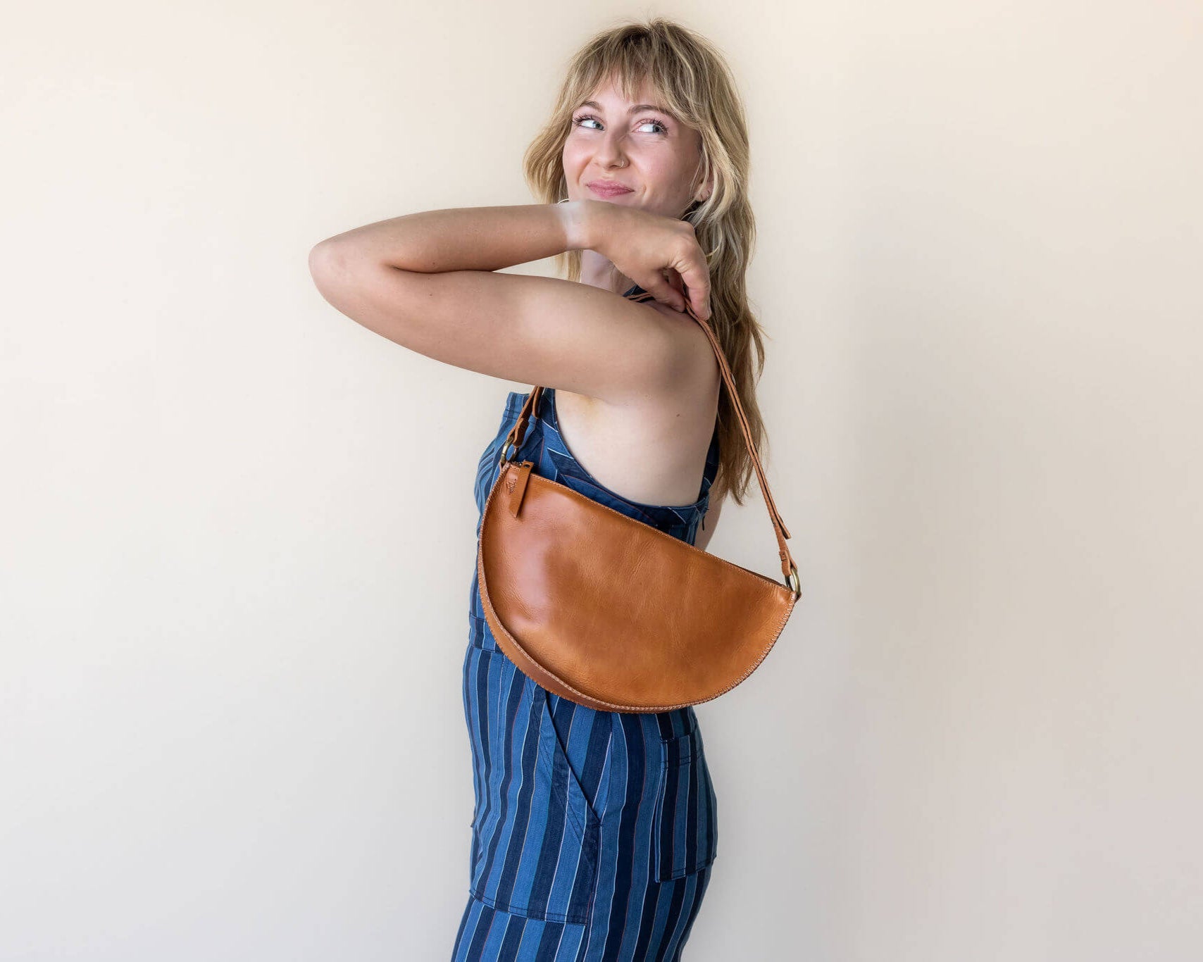 Woman holding a brown leather bag against a plain background