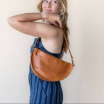 Woman holding a brown leather bag against a plain background