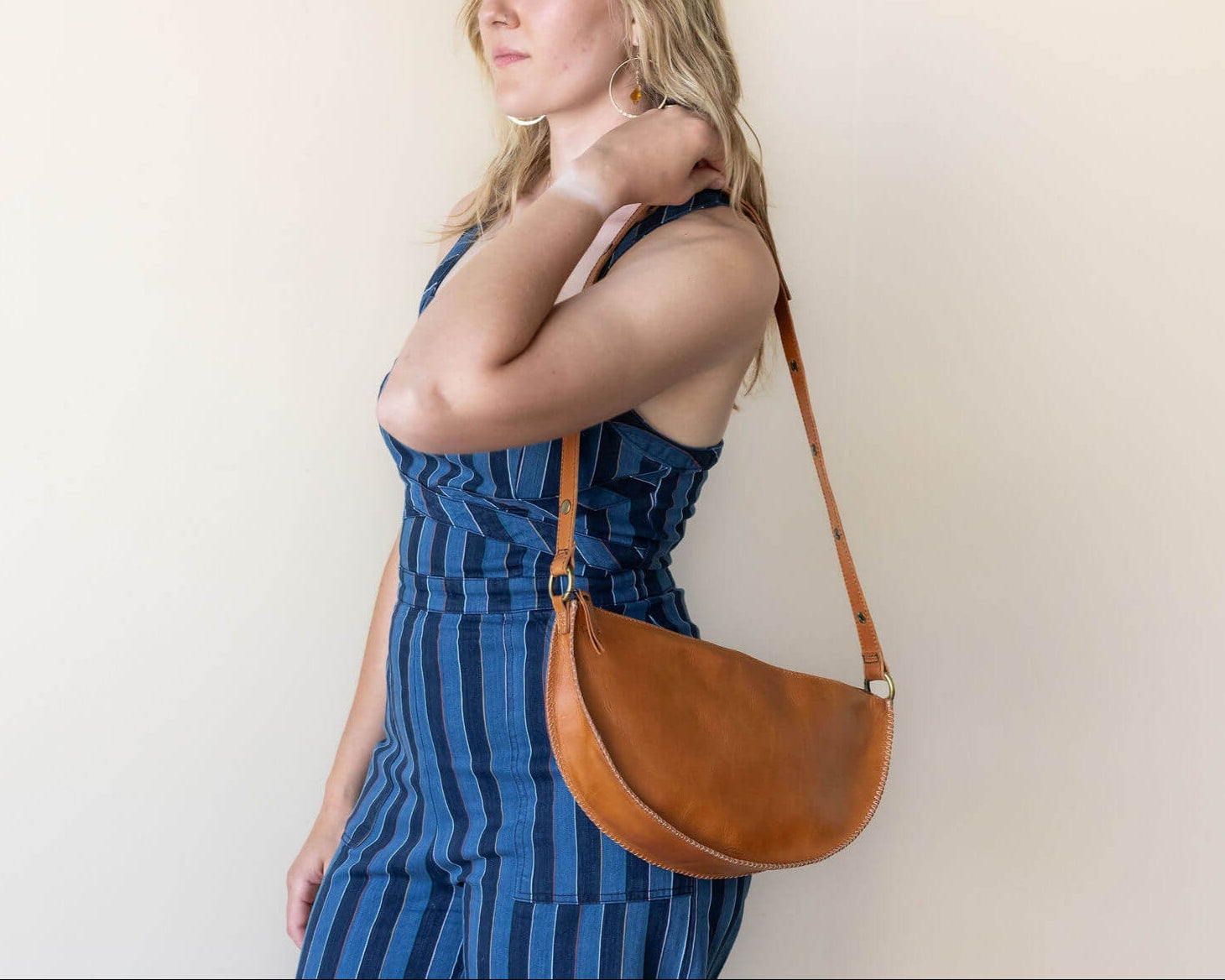Woman wearing a blue striped dress with a brown leather shoulder bag against a plain background