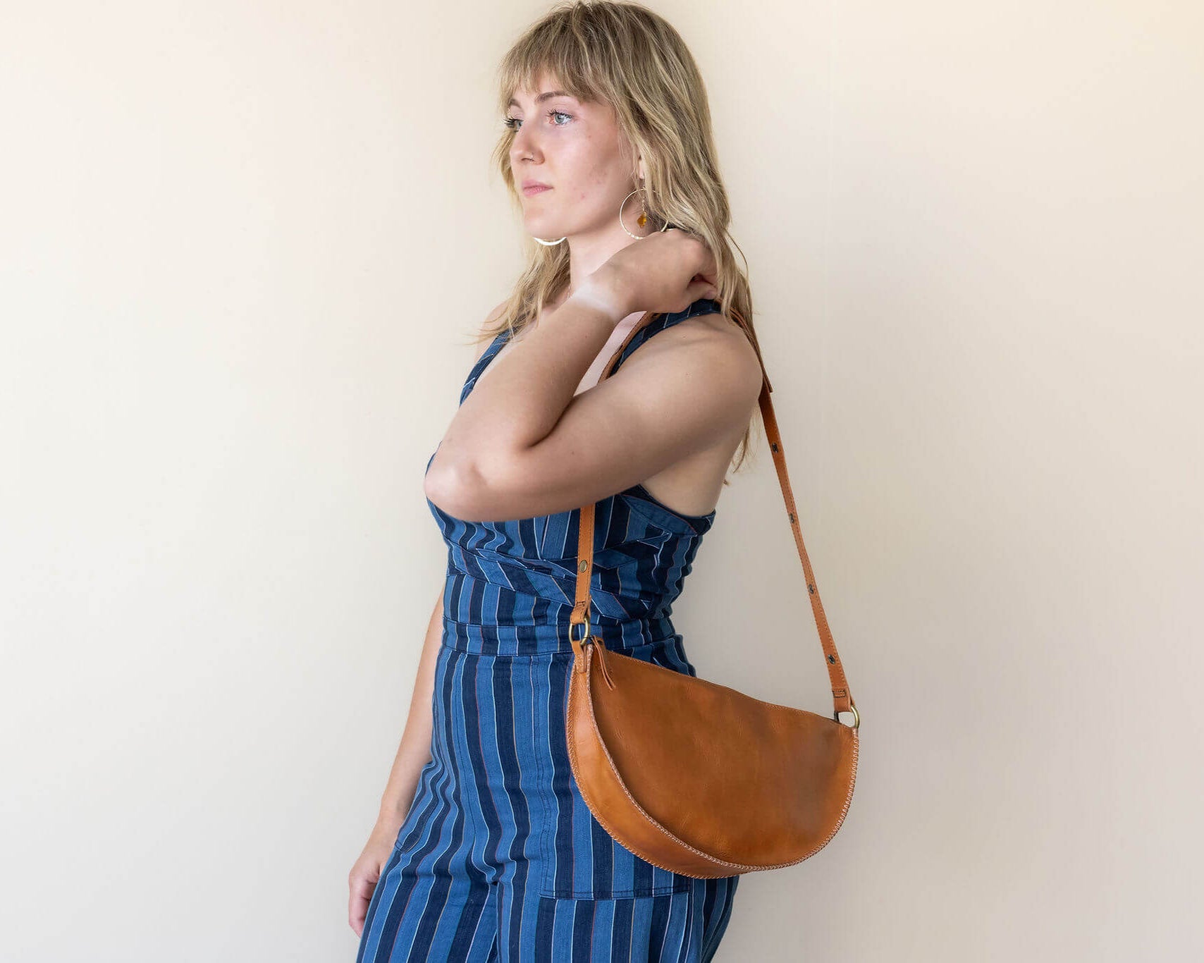 Woman wearing a blue striped dress with a brown leather shoulder bag against a plain background
