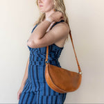 Woman wearing a blue striped dress with a brown leather shoulder bag against a plain background