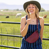 Woman in a striped dress and hat holding a dandelion in a field with animals in the background