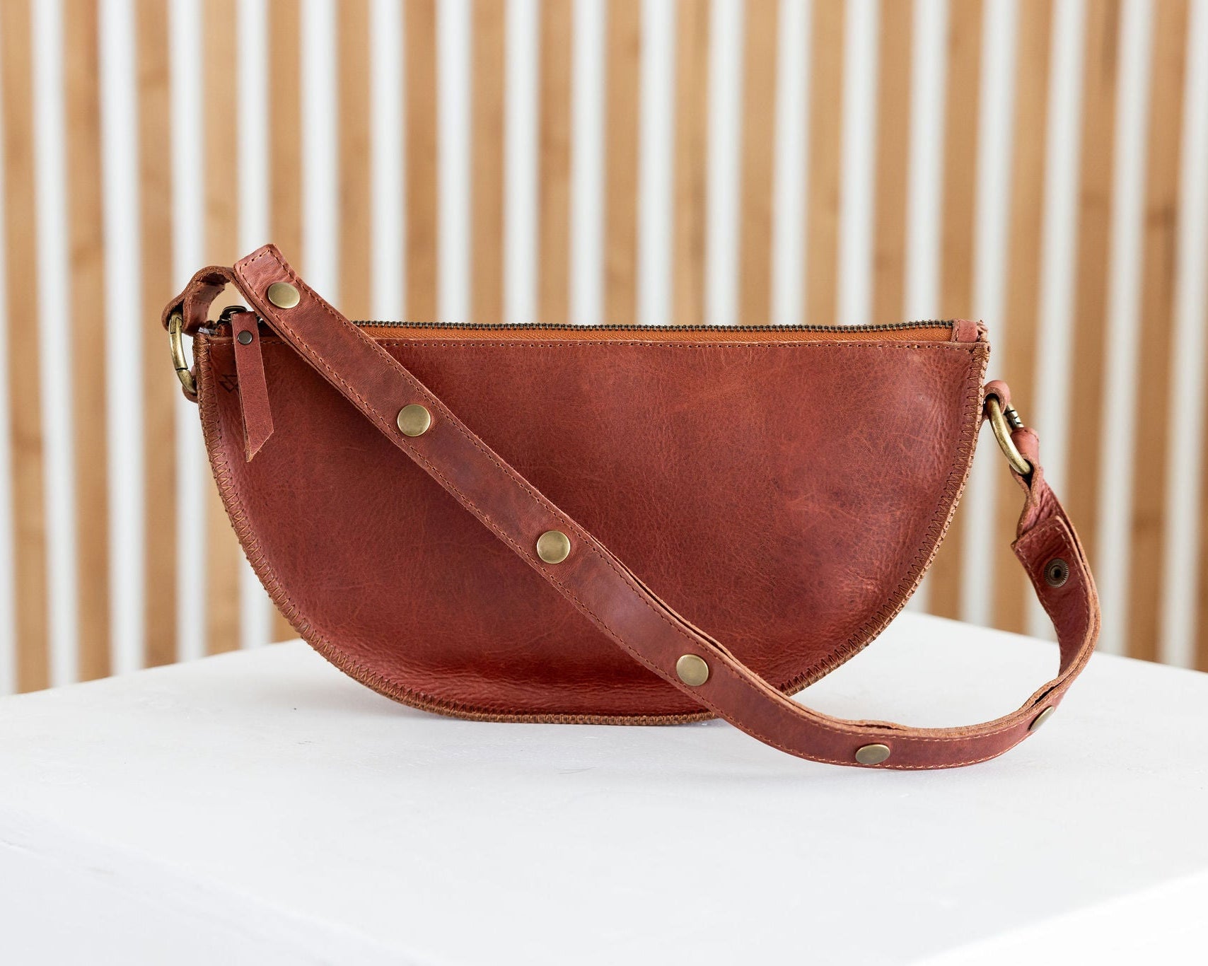 Brown leather handbag on a white surface with a wooden background