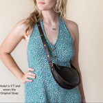 Woman wearing a teal floral dress with a brown leather bag over her shoulder against a plain background.