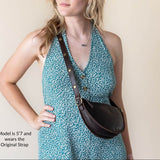 Woman wearing a teal floral dress with a brown leather bag over her shoulder against a plain background.