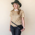 Woman wearing a patterned blouse, jeans, and a hat against a plain background