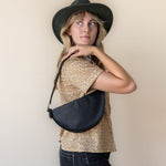 Woman wearing a black hat and carrying a black bag against a beige background