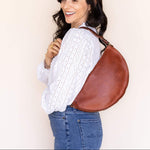 Woman carrying a brown leather bag against a plain background