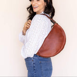 Woman carrying a brown leather bag against a plain background