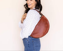 Woman carrying a brown leather bag against a plain background