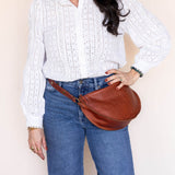 Person wearing a white sweater and blue jeans with a brown leather bag on a beige background