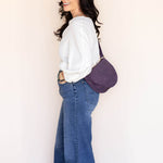 Woman wearing a white shirt and blue jeans with a purple bag against a plain background