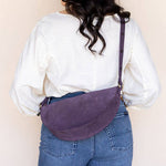 Person wearing a white shirt and blue jeans with a purple bag over their shoulder against a plain background