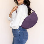 Woman wearing a purple crossbody bag against a plain background
