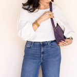 Woman holding a purple handbag against a plain background