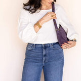 Woman holding a purple handbag against a plain background