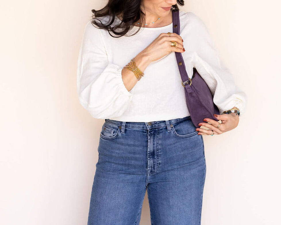 Woman holding a purple handbag against a plain background