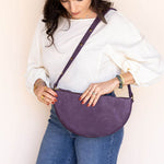 Woman holding a purple crossbody bag against a plain background