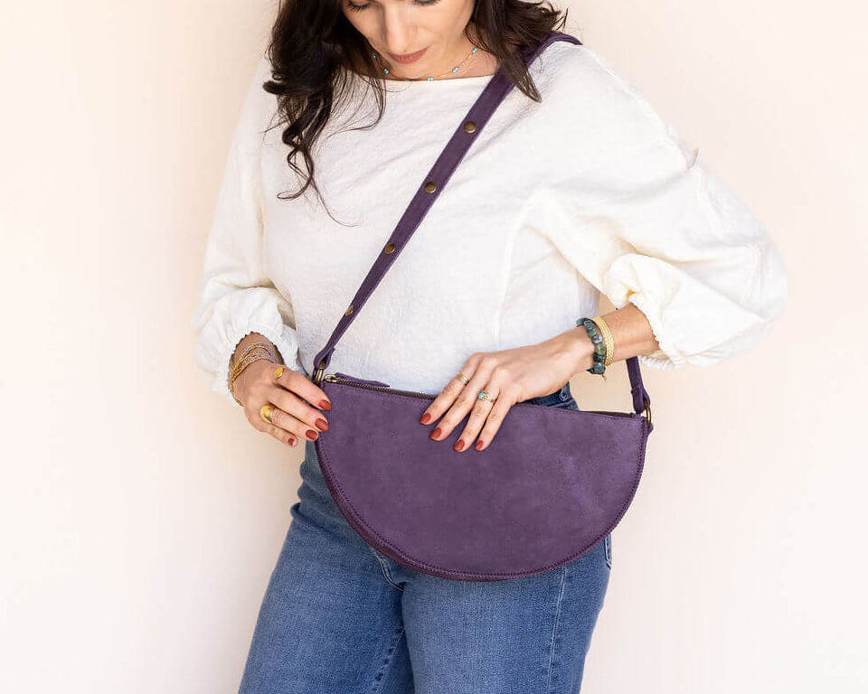 Woman holding a purple crossbody bag against a plain background