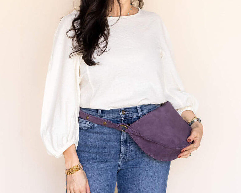 Woman wearing a white shirt, blue jeans, and a purple waist bag against a plain background
