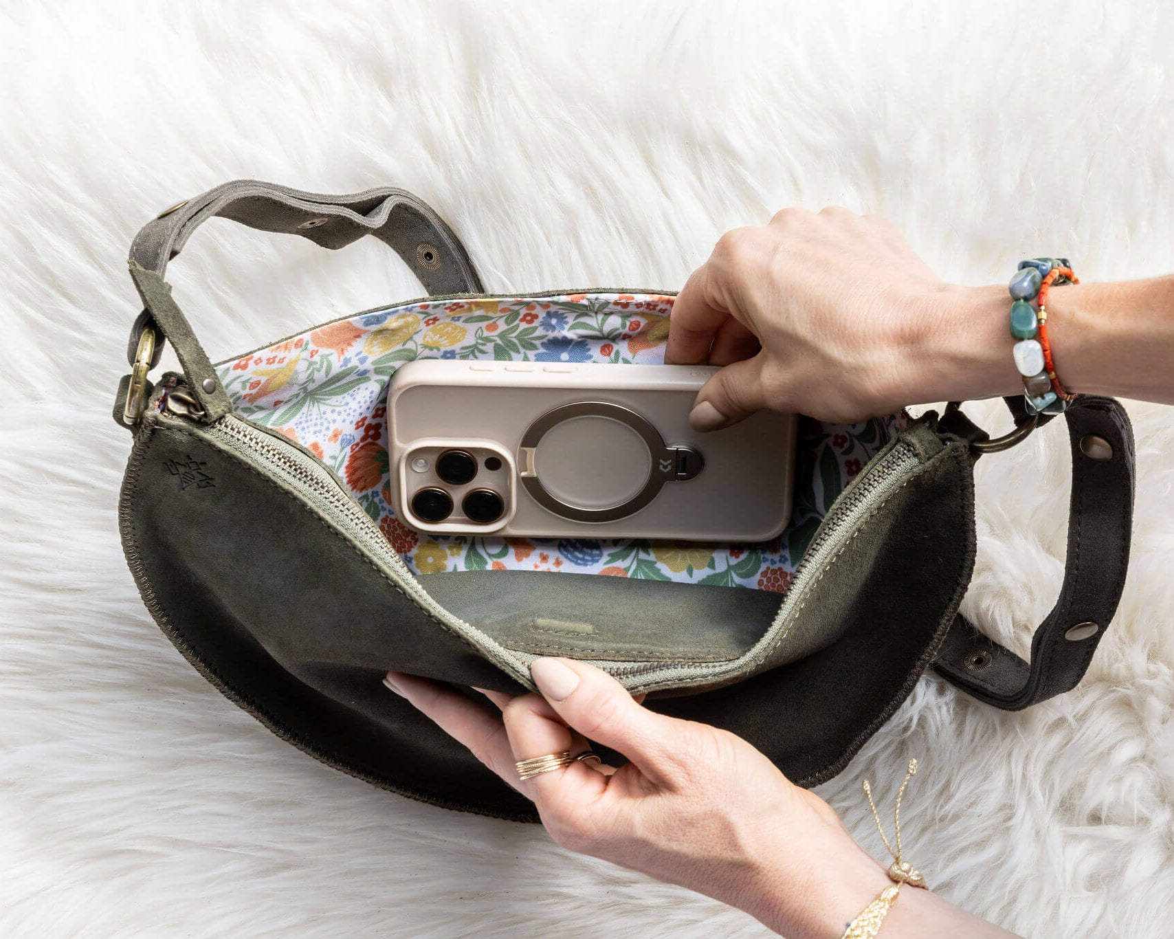 Person placing a phone into a handbag on a white surface