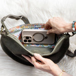 Person placing a phone into a handbag on a white surface