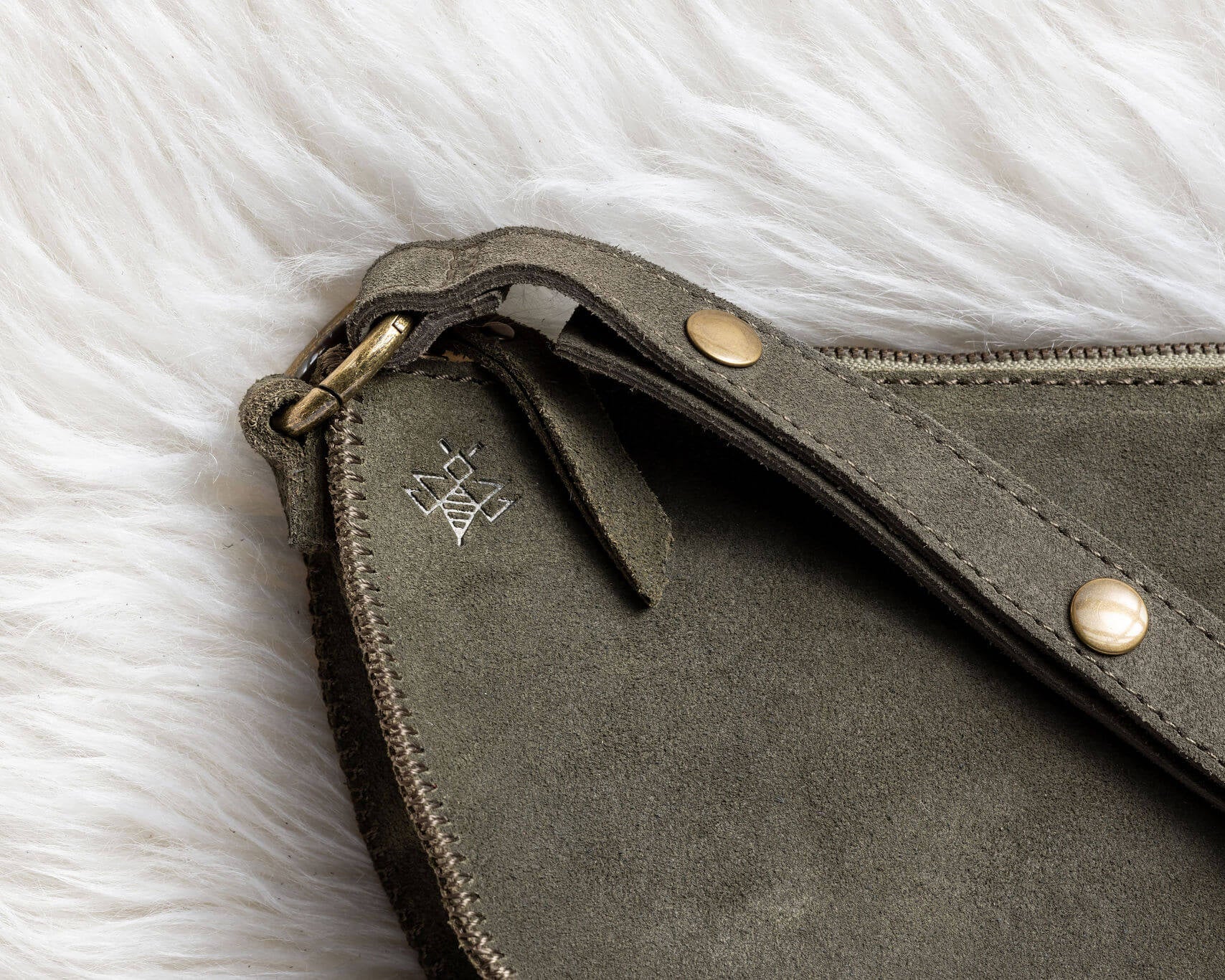 Close-up of a gray leather clutch bag with gold accents on a white fur surface
