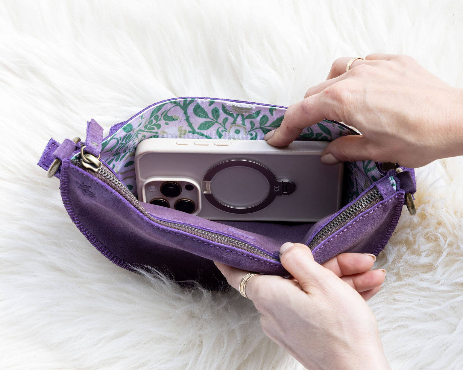 Person placing a phone with a purple case into a purple pouch on a white surface