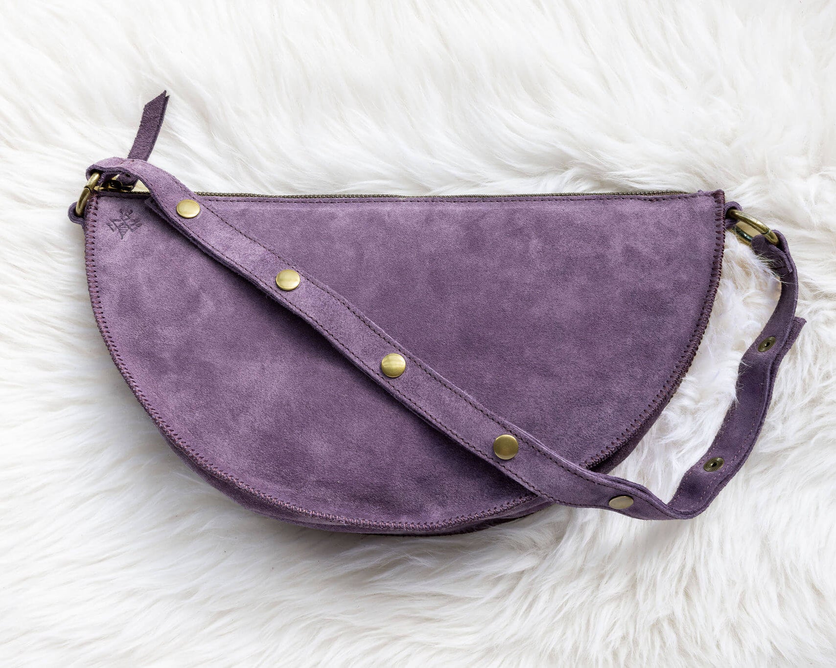 Purple half-moon bag with gold buttons on a white fluffy background