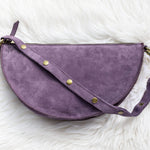 Purple half-moon bag with gold buttons on a white fluffy background