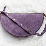 Purple half-moon bag with gold buttons on a white fluffy background