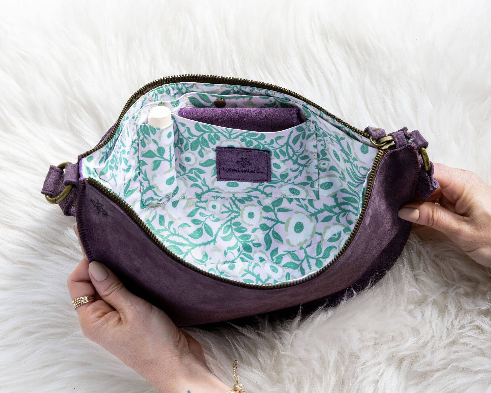 Purple bag with floral interior lining held by a person on a white fur surface