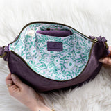 Purple bag with floral interior lining held by a person on a white fur surface