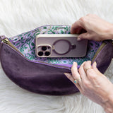 Purple pouch with floral interior containing a phone case, held by hands on a white fluffy surface.