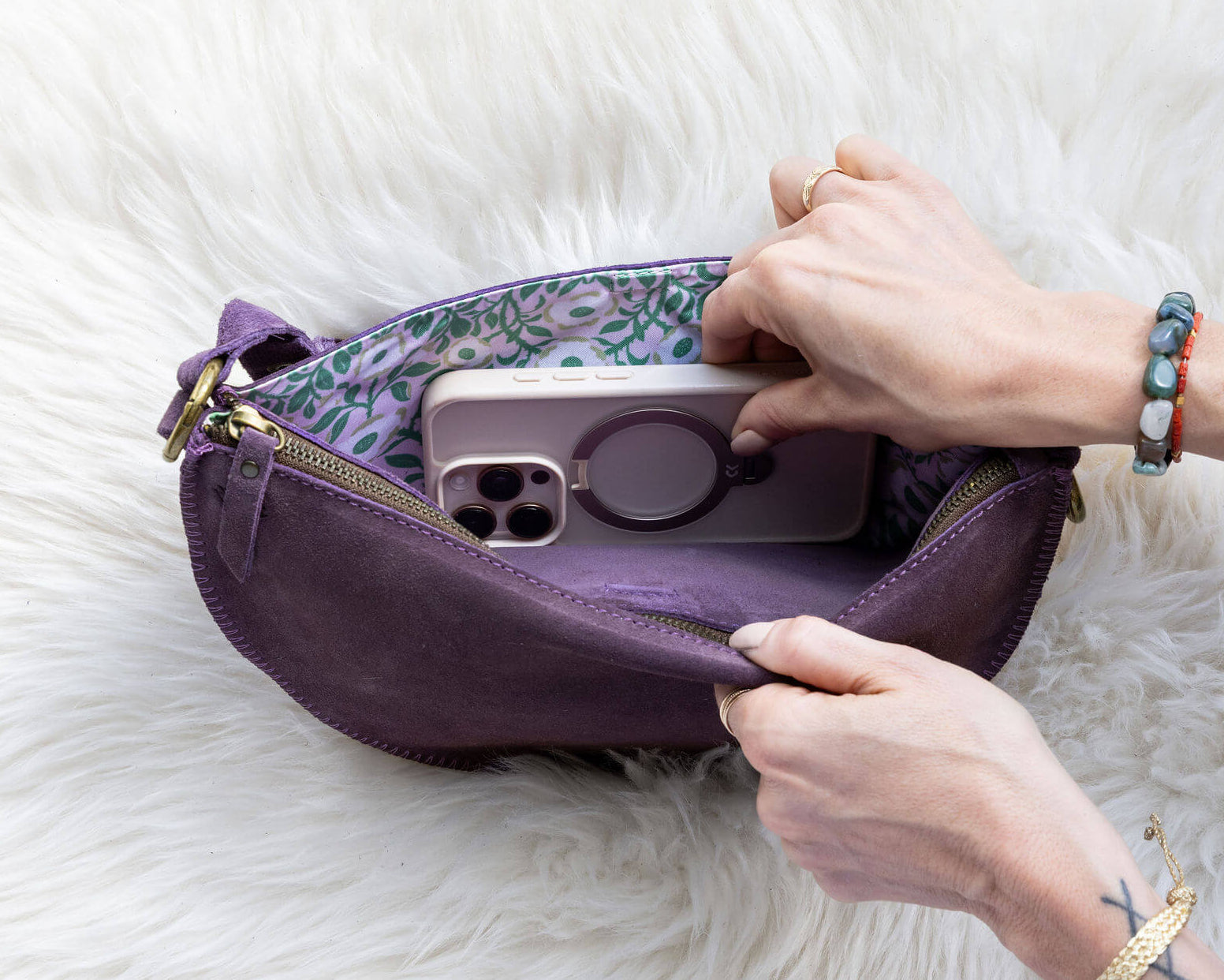 Person placing a phone into a purple pouch on a white fur surface