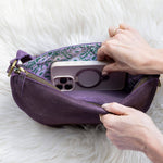 Person placing a phone into a purple pouch on a white fur surface