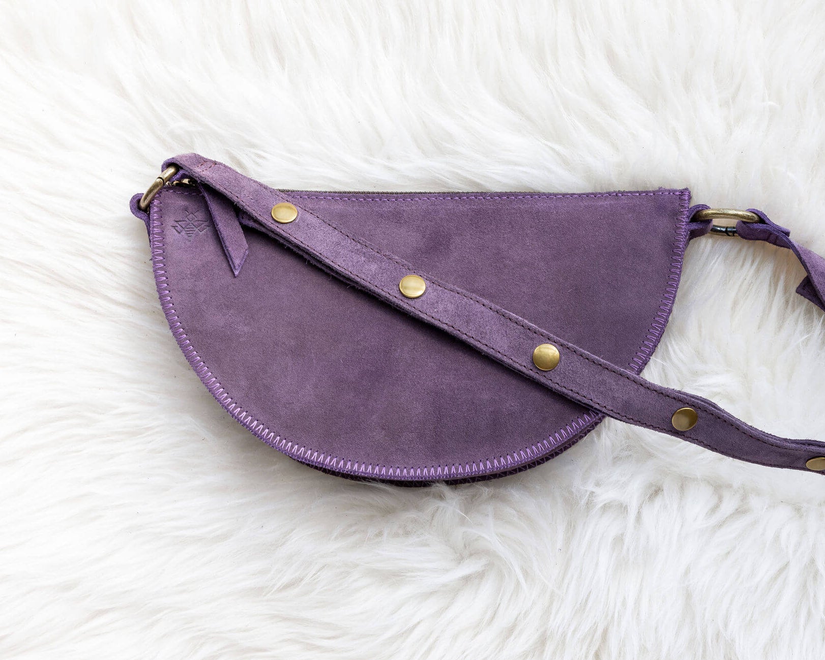 Purple leather bag with gold studs on a white fluffy surface