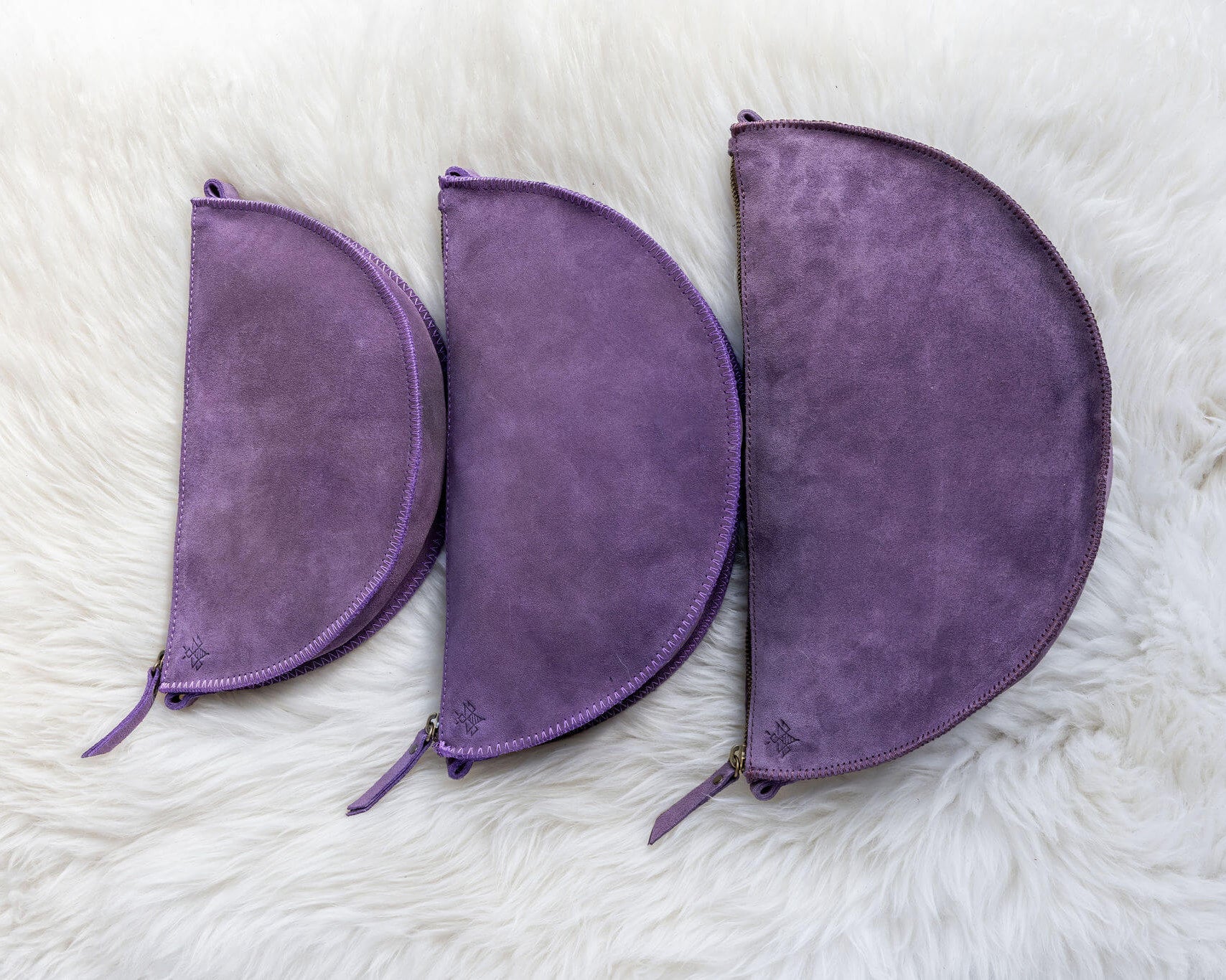 Three purple suede pouches of different sizes on a white fur surface