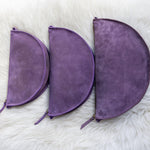 Three purple suede pouches of different sizes on a white fur surface