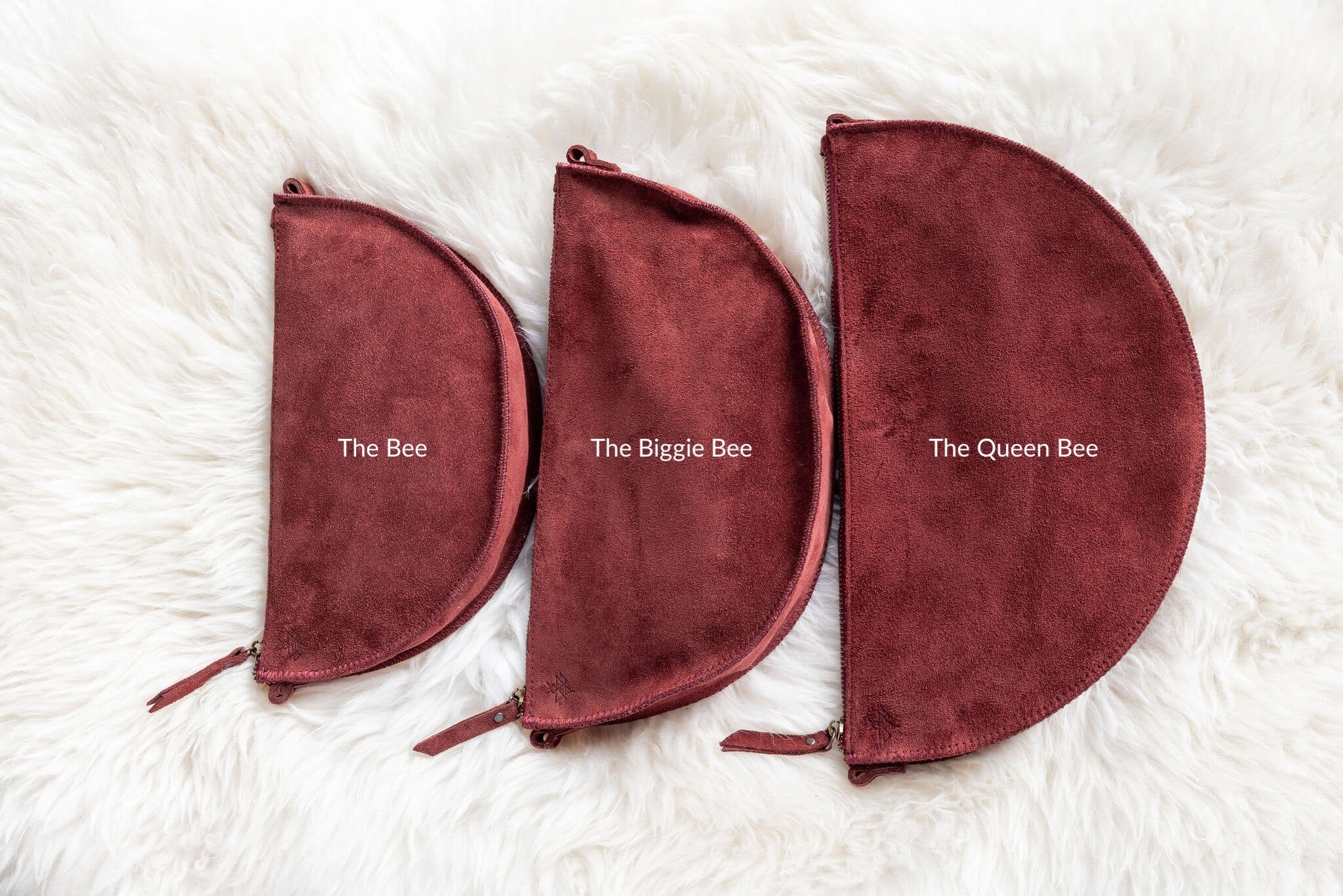 Three maroon pouches labeled 'The Bee', 'The Biggie Bee', and 'The Queen Bee' on a white fur background.