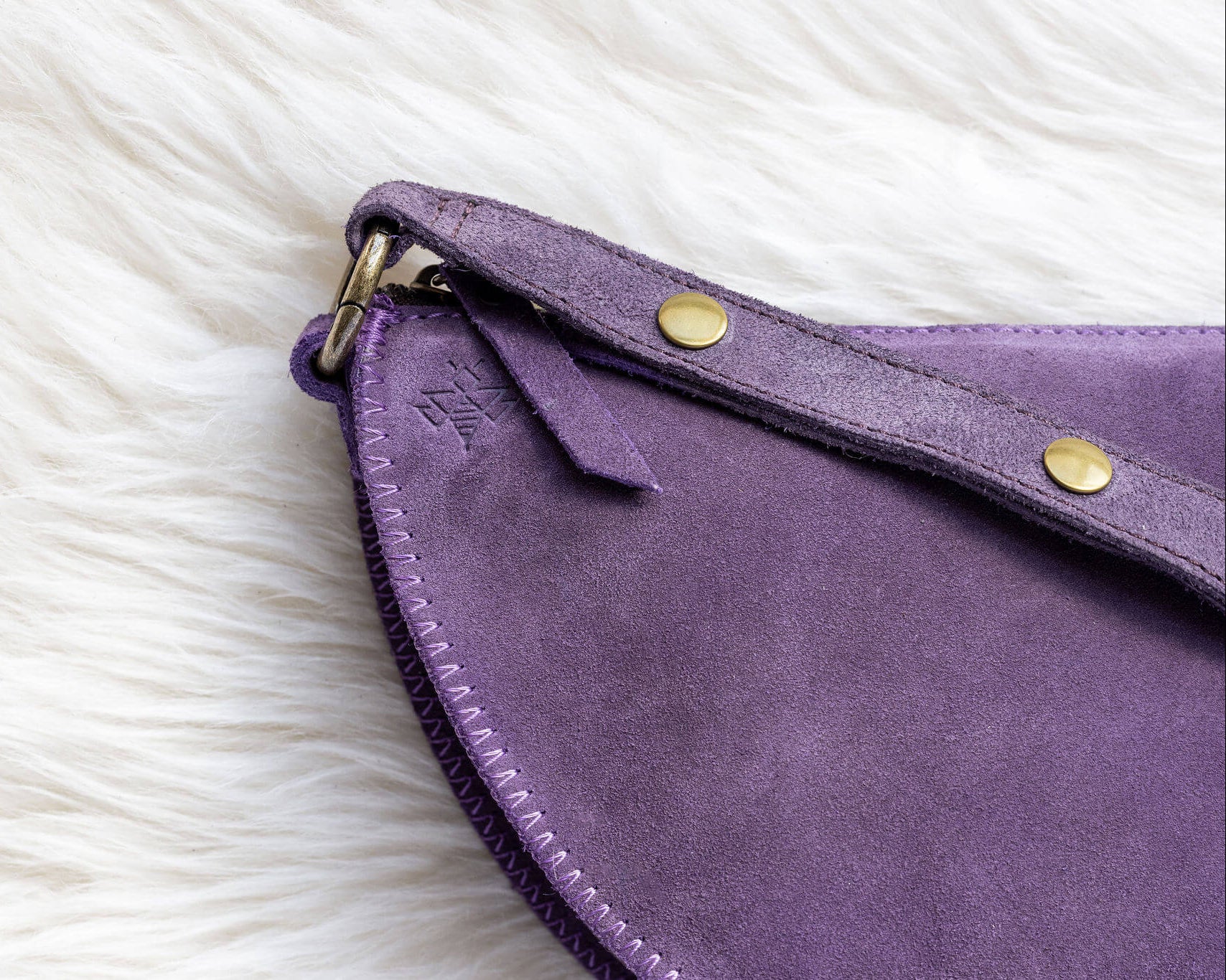 Close-up of a purple suede clutch bag with gold hardware on a white fur surface