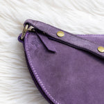 Close-up of a purple suede clutch bag with gold hardware on a white fur surface