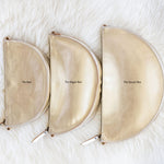 Three gold pouches labeled 'The Box', 'The Baggage Box', and 'The Queen Bee' on a white fluffy surface.