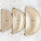 Three gold pouches labeled 'The Box', 'The Baggage Box', and 'The Queen Bee' on a white fluffy surface.