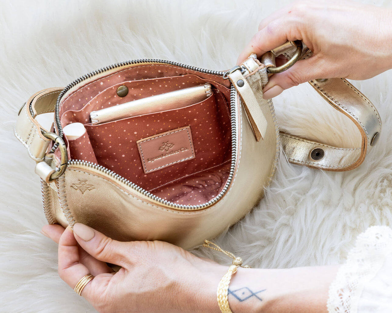Beige handbag with gold accents held open by a hand on a white fur surface