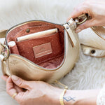 Beige handbag with gold accents held open by a hand on a white fur surface