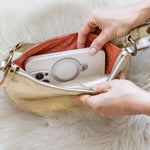 Person opening a beige handbag on a white fur surface