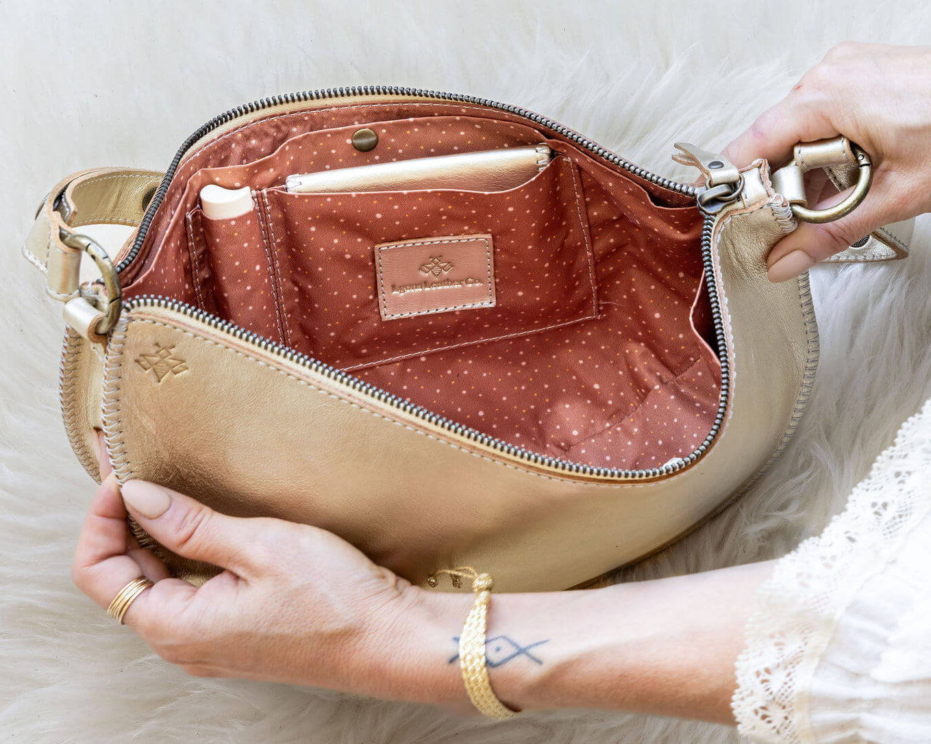 Close-up of a beige handbag with a gold zipper on a white fur background